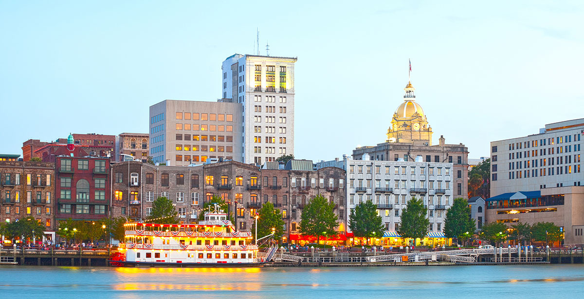 Savannah Georgia USA, skyline of historic downtown at sunset with illuminated buildings and steam boats